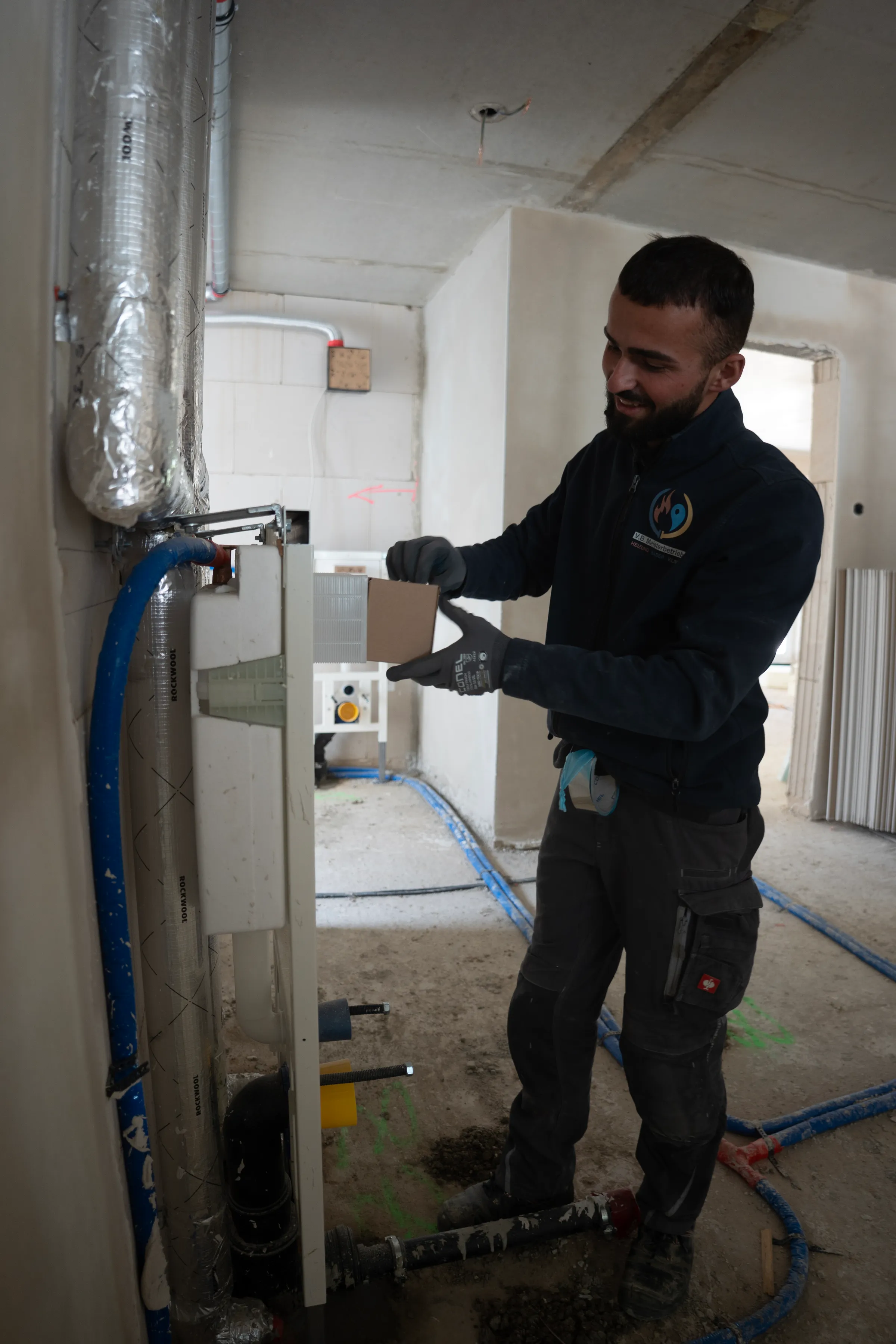 Monteur arbeitet lächelnd an Heizungsanlage im Rohbau