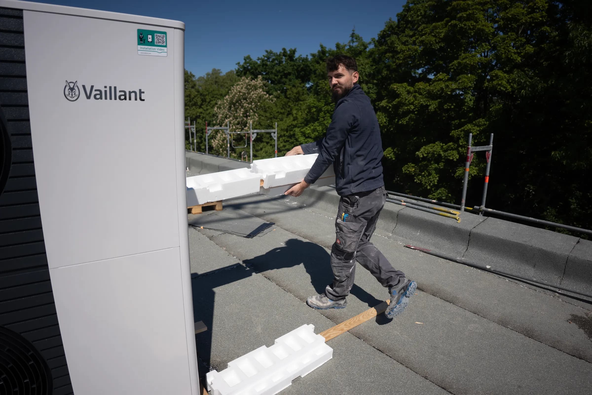 Monteur trägt Material neben Vaillant Wärmepumpe auf Dach