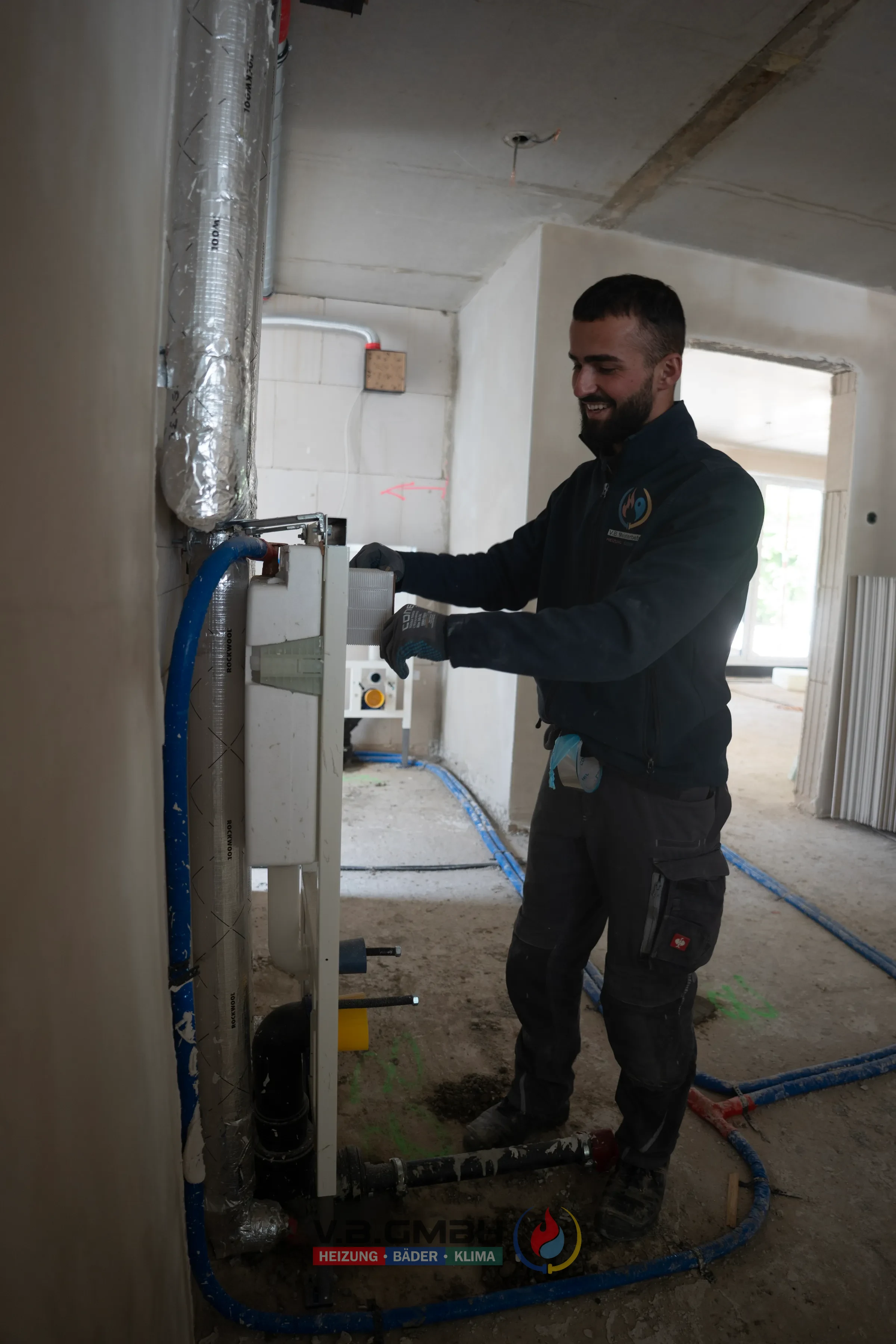 Monteur arbeitet lächelnd an Heizungsanlage im Neubau
