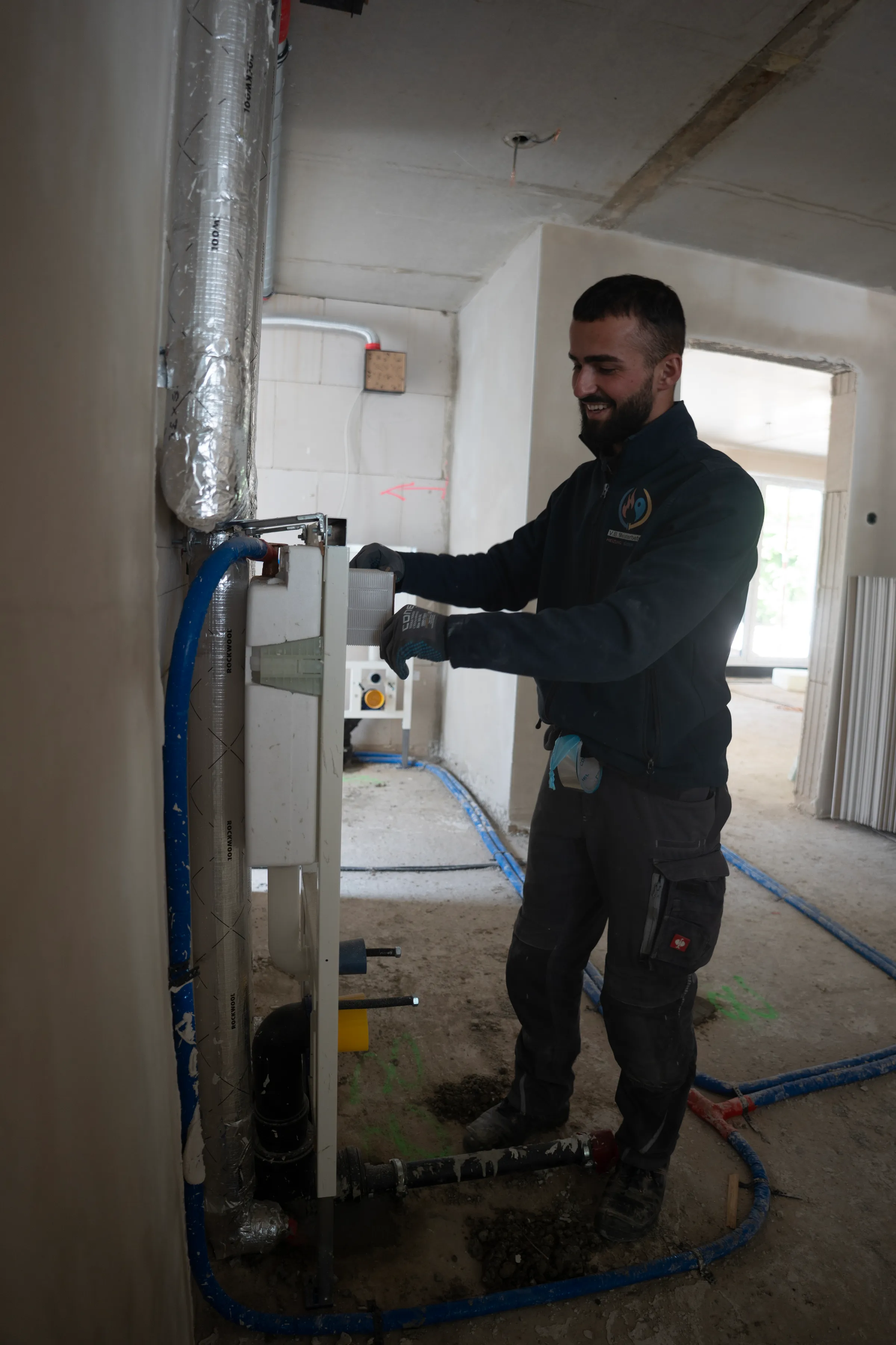 Monteur arbeitet lächelnd an Heizungsanlage im Neubau