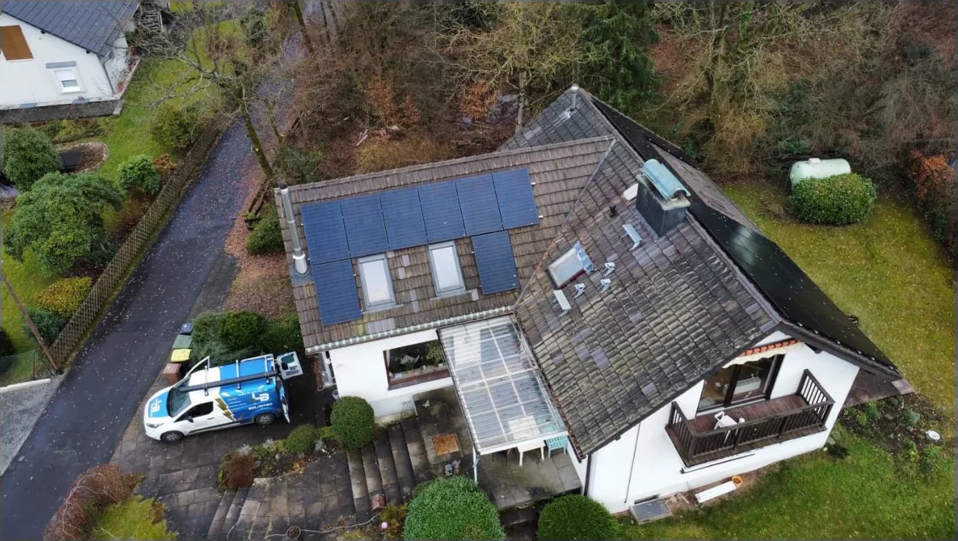 Luftaufnahme eines Einfamilienhauses mit Photovoltaik-Anlage und einem Fahrzeug von LB-Solartec in der Einfahrt