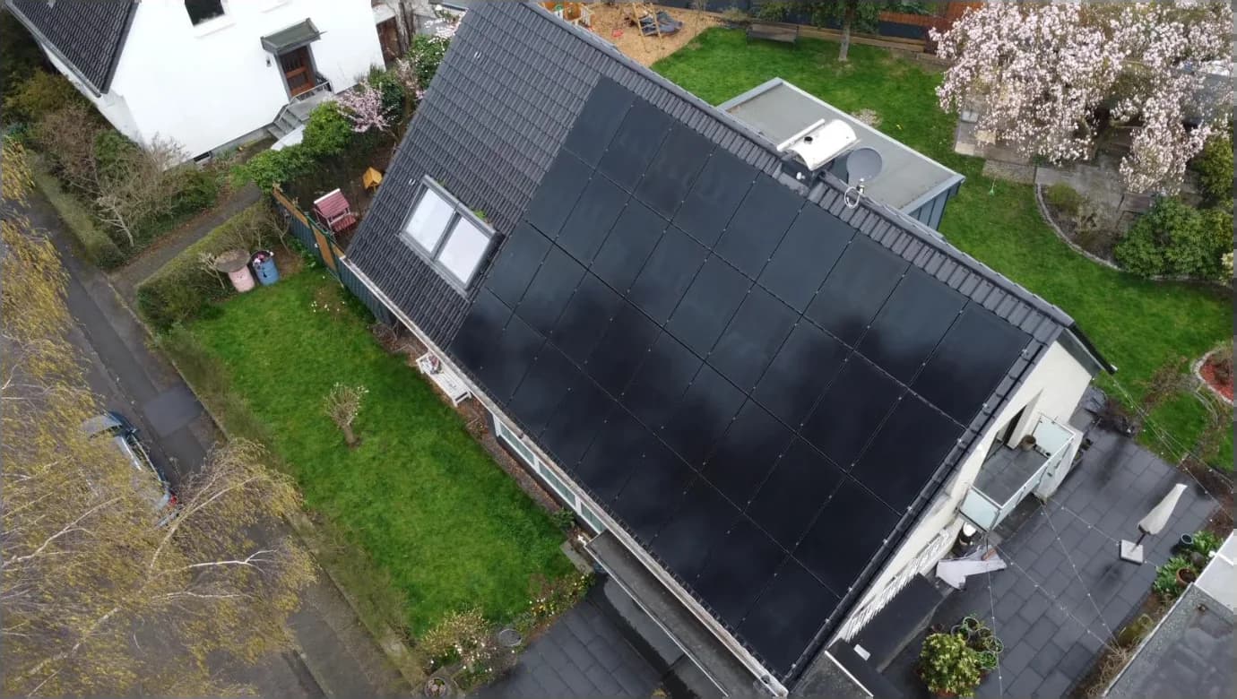 Luftaufnahme einer Photovoltaik-Anlage mit schwarzen Solarmodulen auf dem Satteldach eines Einfamilienhauses