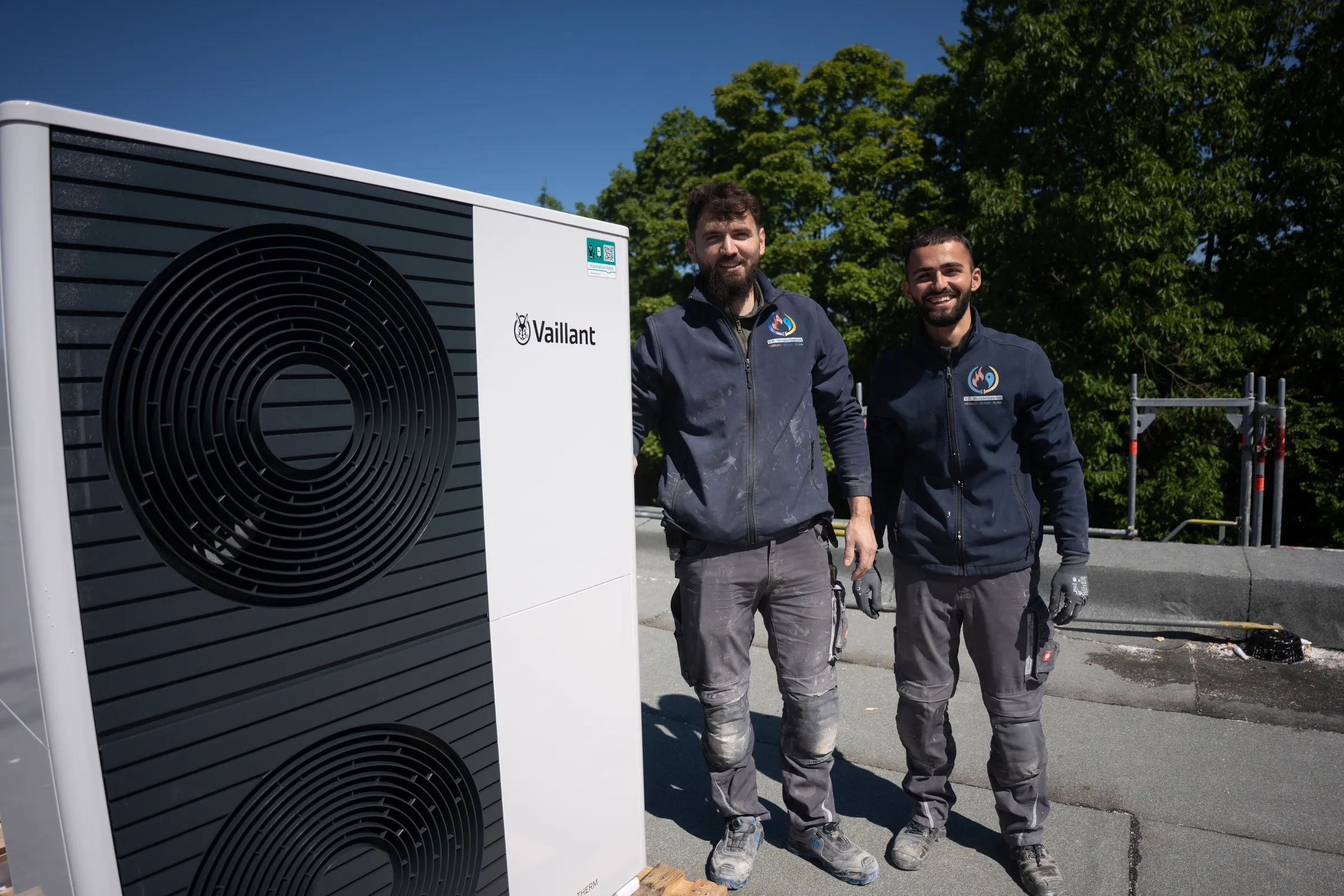 Zwei Monteure lächeln neben Vaillant Wärmepumpe auf Flachdach