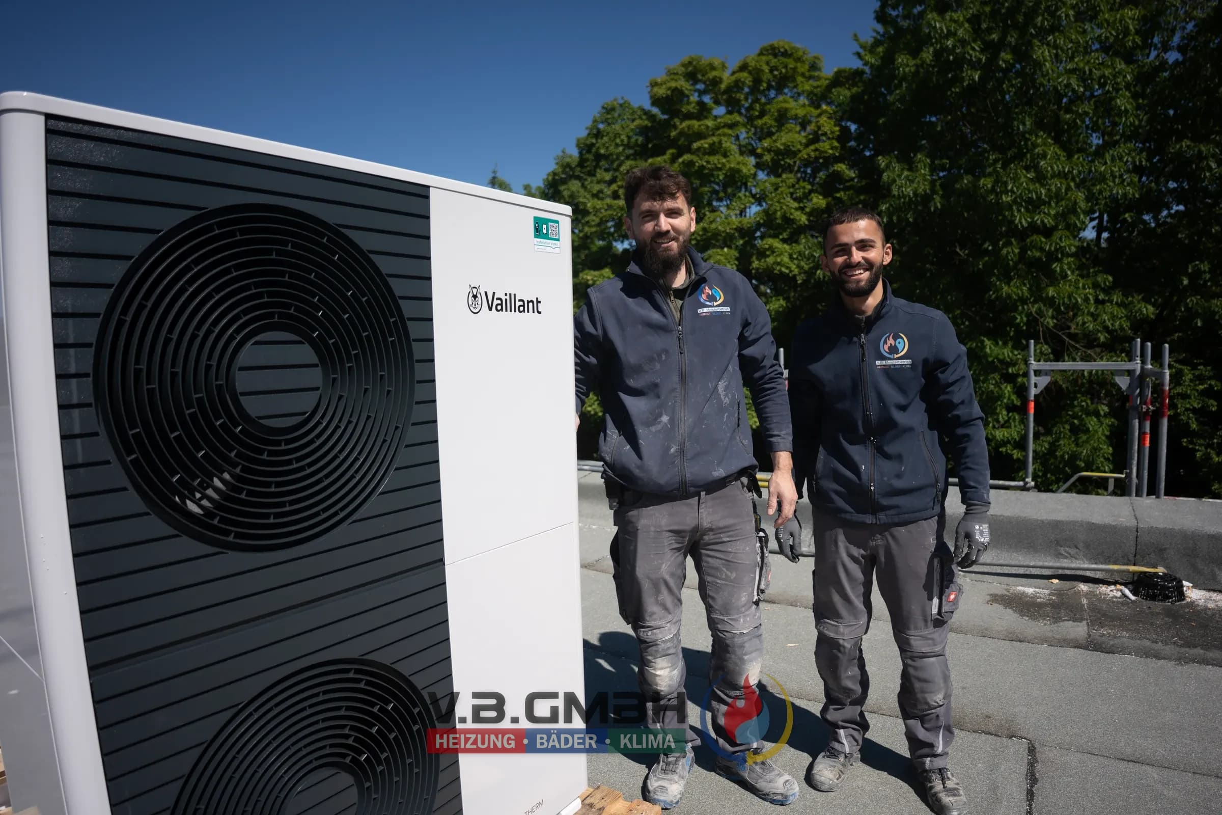 Zwei Monteure lächeln neben Vaillant Wärmepumpe auf Flachdach
