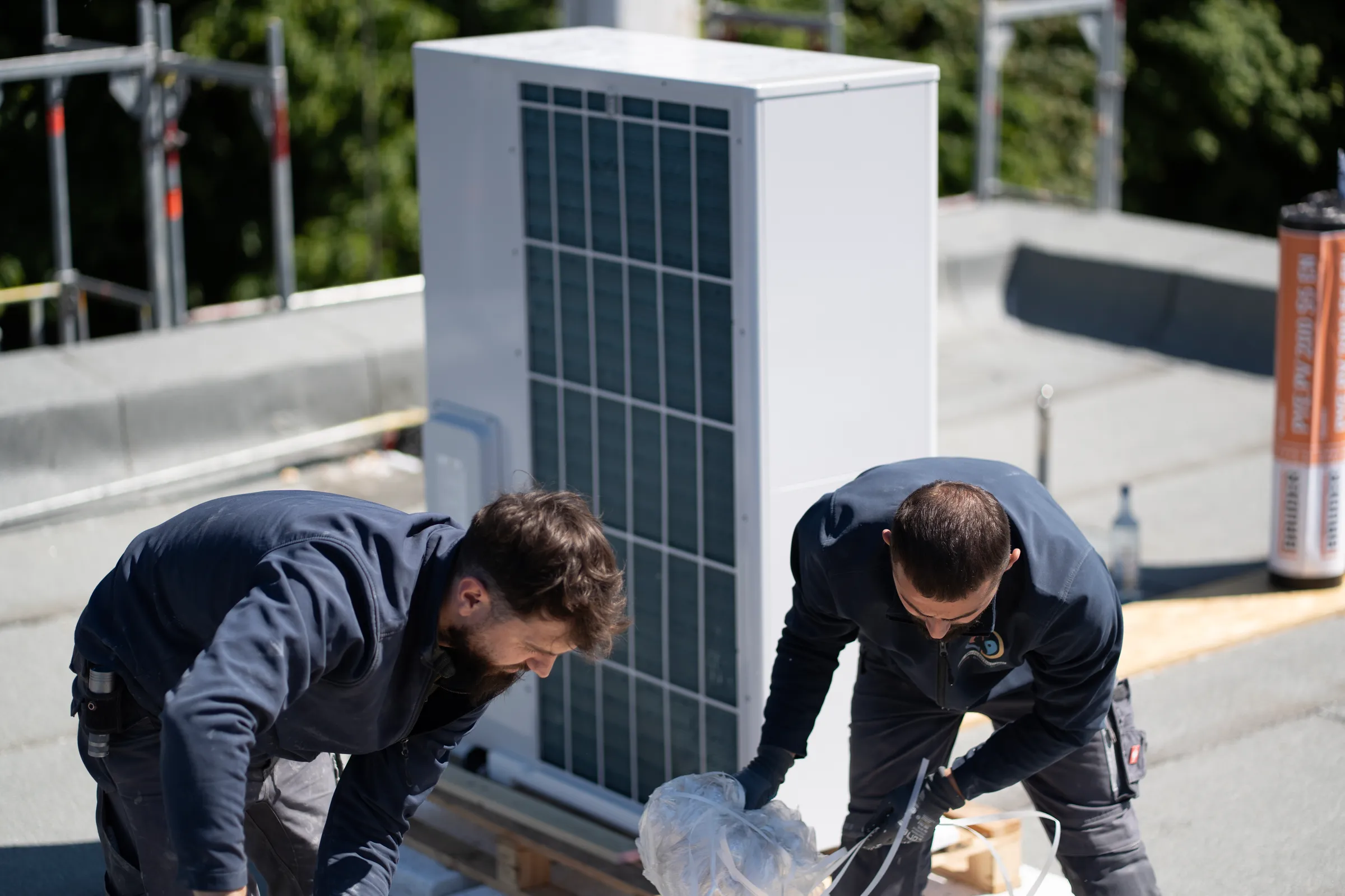 Zwei Monteure installieren gemeinsam Wärmepumpe auf Flachdach
